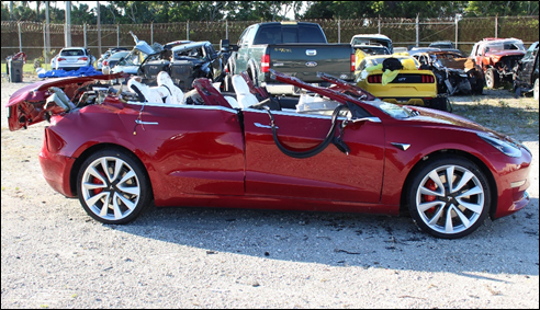 Photo of Tesla Model 3 with extensive roof damage photographed postcrash at tow yard.