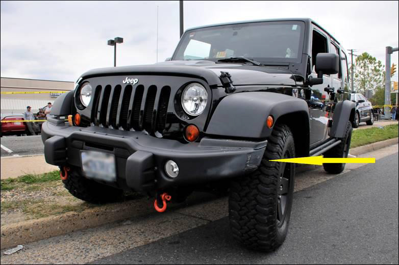 Photograph showing minor contact damage (arrow) to left front bumper of SUV.