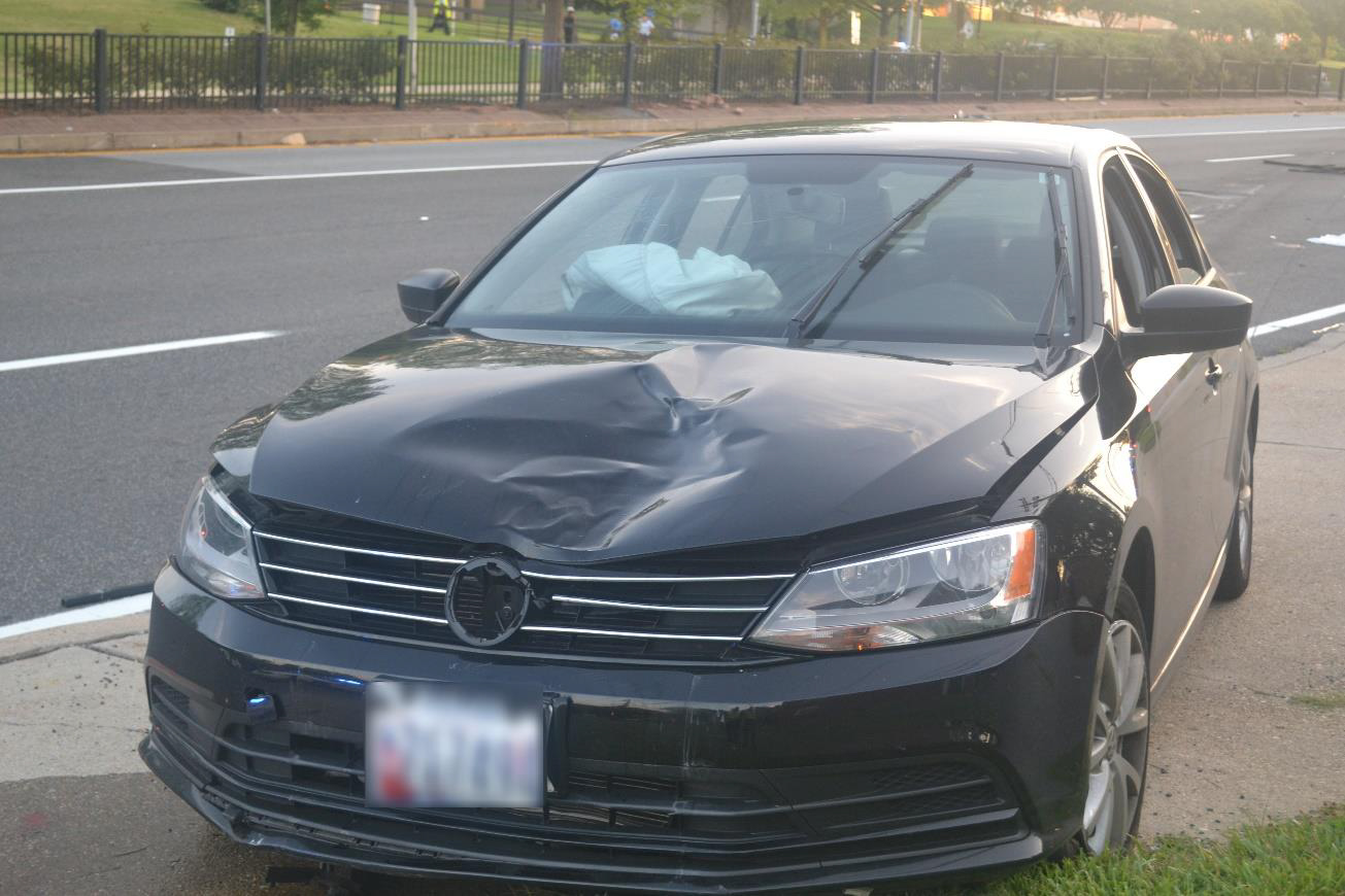 Photograph of crash car showing contact damage to hood. Inflated passenger air bag is visible behind windshield.