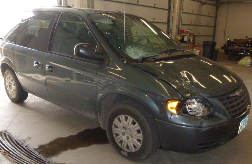 Photograph of minivan showing damage to right bumper, headlight assembly, hood, and windshield.