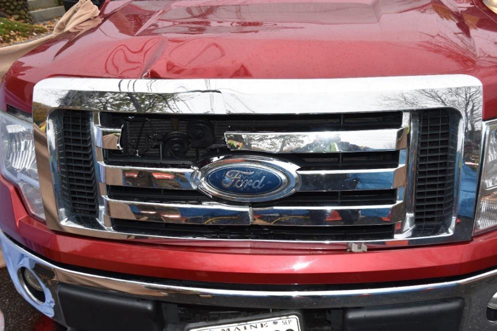 ​Closeup photo of crash vehicle showing damage to hood and grille.
