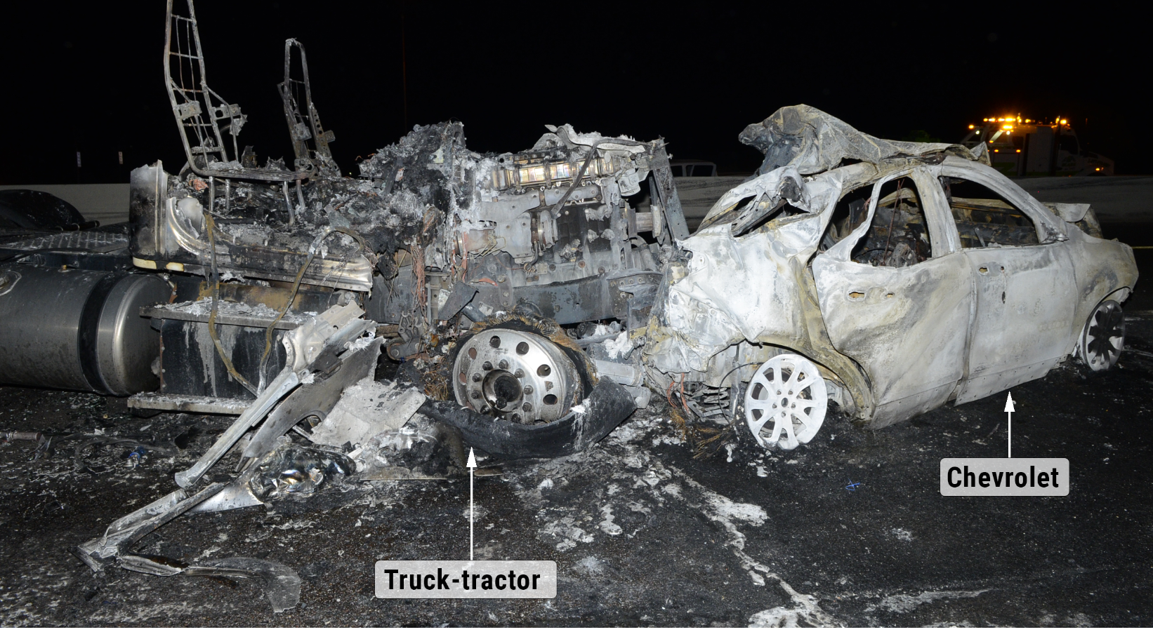 On-scene, postcrash photo of the severely collision-damaged and burned-out remnants of the truck-tractor and the Chevrolet, seen