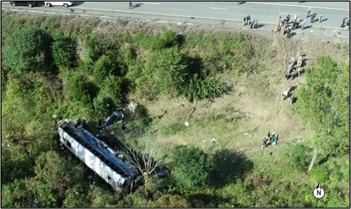 An aerial view of the motorcoach at final rest on its left side at the bottom of the median.