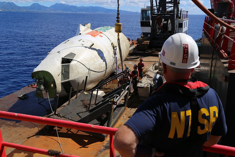 Photo of the forward section of the fuselage of TransAir B-737 as it's recovered onto a barge from the Pacific Ocean